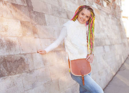Beautiful girl with colored dreadlocks summer sunny day in a white jacket with a vintage brown bag...