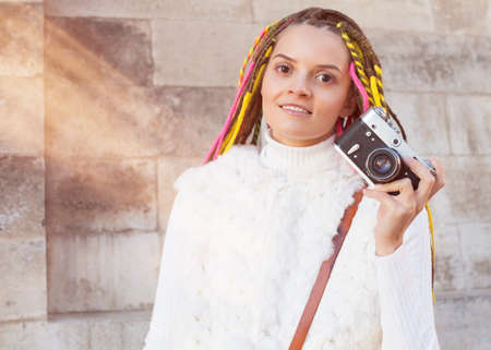Beautiful girl with colored dreadlocks summer sunny day in a white jacket with a vintage brown bag over her shoulder holding in her hand vintage cameraの写真素材