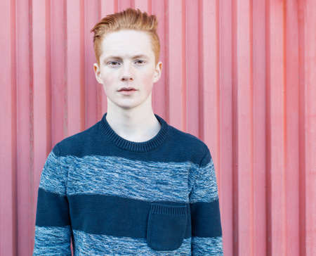 Young redhead man in a sweater and jeans standing next to red wallの写真素材
