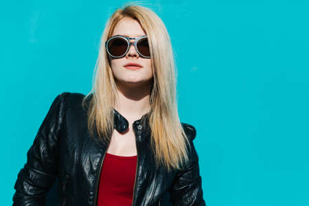 Portrait of a young beautiful blonde girl in huge sunglasses on the background of turquoise wall sunny summer dayの写真素材