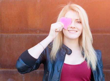 Portrait of a beautiful blonde girl with one hand closes the eyes pink paper heartの写真素材