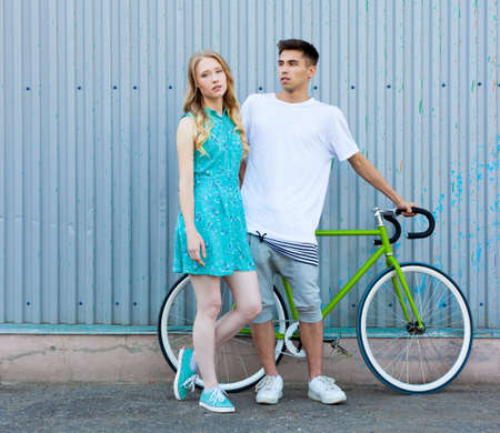 Young happy hipster couple in love meet each other and dating whis bicycle. Pretty blonde caucasian woman with her hispanic boyfriend posing outdoor in summerの写真素材