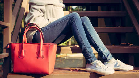 Girl sitting on the stairs with a big red super fashionable handbags in a sweater jeans and sneakers on a warm summer evening. warm colorsの写真素材