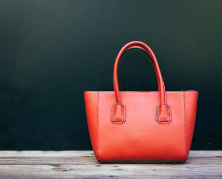 Fashionable beautiful big red handbag standing on a wooden floor on black wall background