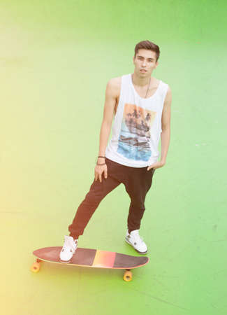 Young male skateboarder standing on longboard on a warm summer evening. Skateboard ramp
