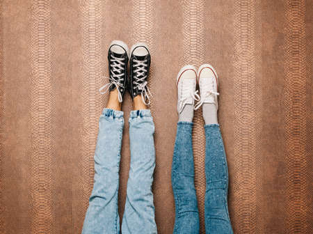 Young fashion couple's legs in jeans and sneakers feet up on wallの写真素材
