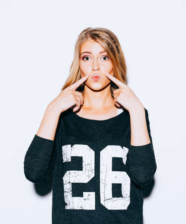 Beautiful young blond girl posing in Sweatshirt and white shorts and red lips kiss does. She points...