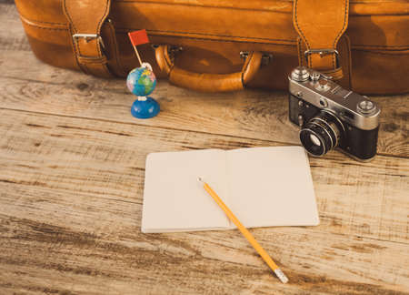 Suitcase, nootbook, pencil, flag, vintage camera on wooden plancs. Aim, attainment, target, tourism,...