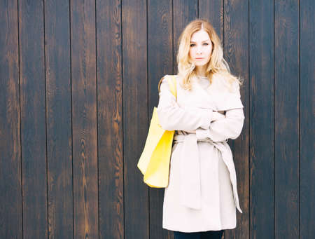 Fashionable beautiful big yellow handbag on the arm of the girl in a fashionable coat, posing near the wall. Warm colorの写真素材