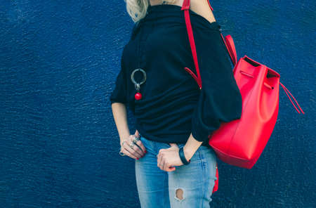 Fashionable beautiful big red backpack on the arm of the girl in a fashionable jeans, posing near...