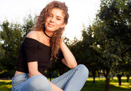 Beautiful young brunette woman with long hair relaxing in the garden on a warm summer evening. Warm...