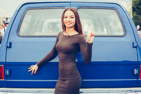 Pretty young girl posing near blue SUV in sexy dress and show victory sign . Sexy Chick. Outdoor.の写真素材