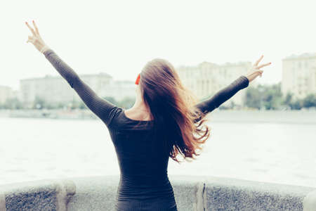 Young woman standing with her back raised his hands, and show victory sign, once free from the city and work. Freedom. Escape. Victory. Conquest. Outdoor.の写真素材