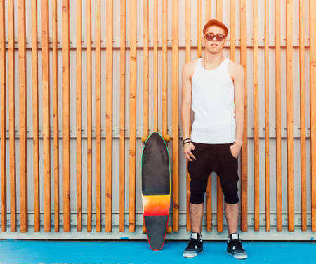 Urban man sunglasses and skateboard posing on wood planks background. Good looking. Cool guy. Wearing white shirt and black pants. Outdoor.の写真素材
