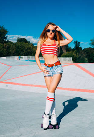 Beautiful blonde girl posing on a vintage roller skates in denim shorts and white, red T-shirt in...