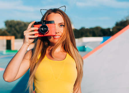 Close up Portrait of beautiful woman with retro hipster camera having fun in skatepark. Warm sunny...