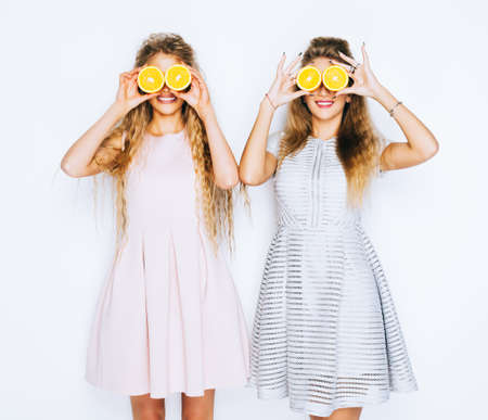 Fashion and beauty. Two stunning beauties girls crazy having fun with slices of oranges closing by them eyes. Conceptの写真素材