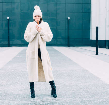 Beautiful girl in a fashionable white coat and knit posing on the street. Srteetstyle. Outdoor.の写真素材