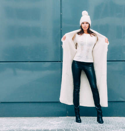 Pretty young woman smiling in a knitted hat and a coat on a background of the Europe city. she shows excellent body. Streetstyle.の写真素材