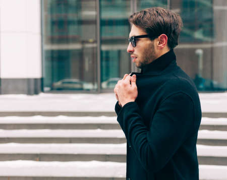 Portrait of young trendy man wearing a black coat with a raised collar. Street style.