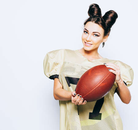 Incredibly beautiful, athletic brunette girl in American football uniform showing the ball inviting...