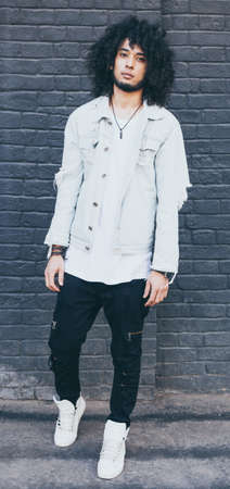 Portrait of handsome young black man with curly afro hair. Outside. Dressed in a jeans jacket, black trousers and high white fashionable sneakers.の写真素材