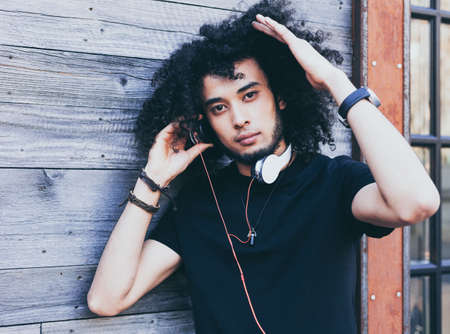 Close up portrait young African American man with an afro hairstyle as DJ. Headphones and red vintage cassette player. Wearing a black outfit. Rockstar. Reggae.の写真素材