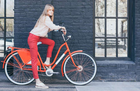 Young pretty sensual blond girl posing outdoor with red vintage bicycle dressed a red Chino Trouser...