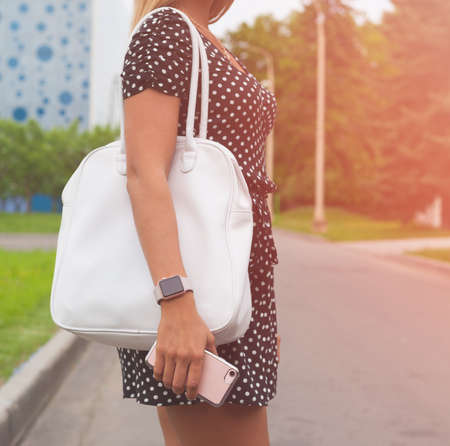 Fashionable beautiful big red handbag on the arm of the girl in a fashionable summer dress, posing on the street a warm summer night. Warm color. Outdoor.の写真素材