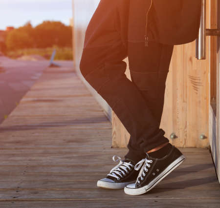 A man in a fashionable black outfit posing at the sunset of a warm summer day in trainers. Part of the body, close-up.の写真素材