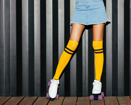 Close-up. Girl posing in a denim skirt, yellow golf on roller skates. Parts of the body. Night...