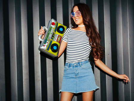 Charming asian girl look at camera in a denim skirt, T-shirt and American sunglasses enjoys music...