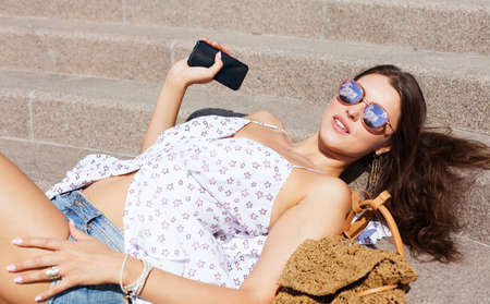 Vacation. The girl in a light outfit sunglasses smartphone and resting lying on the stone steps