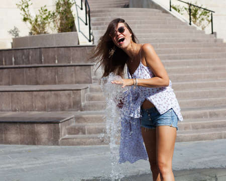 Vacation. A girl in a light outfit sunglasses on a hot summer day playing with a fountain in the park of a European cityの写真素材