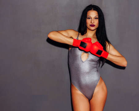 Beautiful brunet girl in red boxing gloves posing on a gray background. The threat and arrogance....
