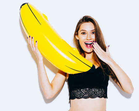 Stunning brunette girl having fun with a huge inflatable banana. On a white background in the studio. Indoor.の写真素材