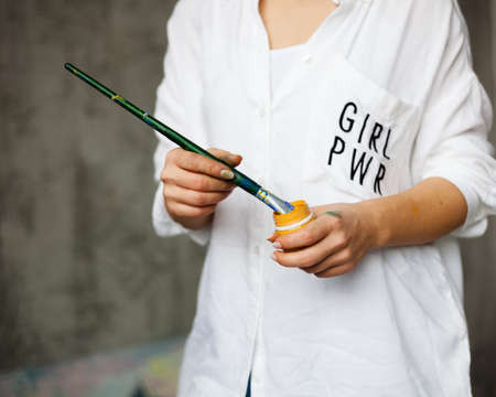 Female power of art. The girl artist is holding a brush and paint. White shirt. The artist gets inspiration.の写真素材