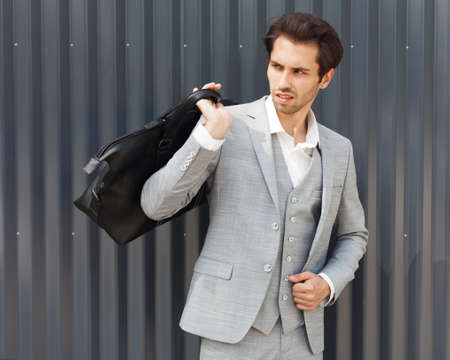 Fashionable portrait. A young man posing in a suit and a cool trendy bag. Outdoor.