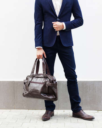 Fashion and Style. A man in a fashionable suit is holding a big trendy bag. Part of the body. Outdoor.の写真素材