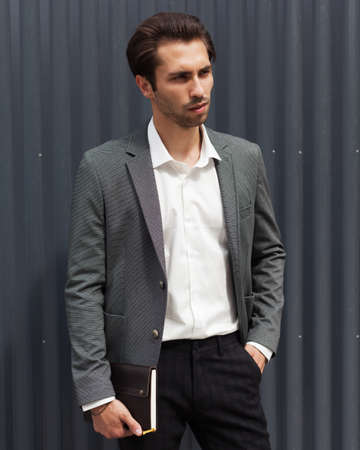 A young man in a fashionable gray jacket with a large black notebook. Fashion and business. Outdoor.