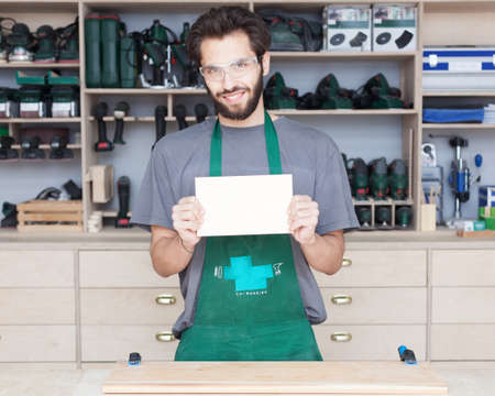 A carpenter. a young bearded hipster in a carpentry shop holds a sign in his hand, a banner.の写真素材