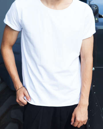 Fashion of the young. A man in a white T-shirt is posing on a summer evening. Cover. Part of the body.の写真素材