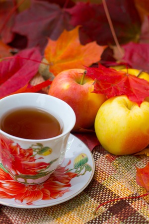 A cup of tea and apples with maple leaves. Autumn tea party, autumn mood, seasonal postcard.の写真素材