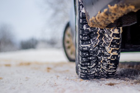 Wheel with spikes on a winter road. Winter road. Snow road. Car on the winter road. Footprints in...