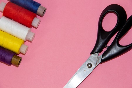 Colored threads and scissors isolated on a pink background. Place under the text. Banner with...