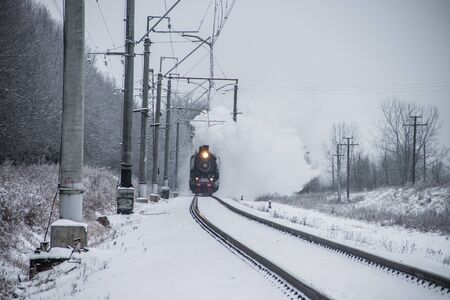 Old locomotive rides by rail in winter. Public transport. Passenger transportation. Russian...
