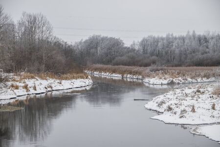 Winter landscape on the river. Snow picture. Snow and river. Cloudy snow day. Freezing dayの写真素材