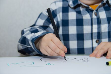 The boy draws felt-tip pens on paper. Drawing. Little boy. Children's drawing. Developmental activities. Colored markersの写真素材