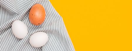 Chicken eggs on a kitchen towel on a yellow background . Concept of farm and home products. Banner with space for text. Foodの写真素材