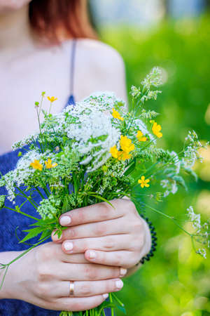A bouquet of wild flowers in women's hands . Bouquet of wildflowers. Soft female hands. Article about collecting flowers. Yellow and white live flowers. Bouquetの写真素材